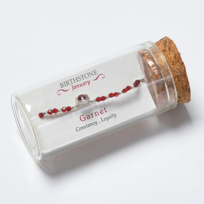 Garnet bracelet in a glass bottle with cork lid on a white background