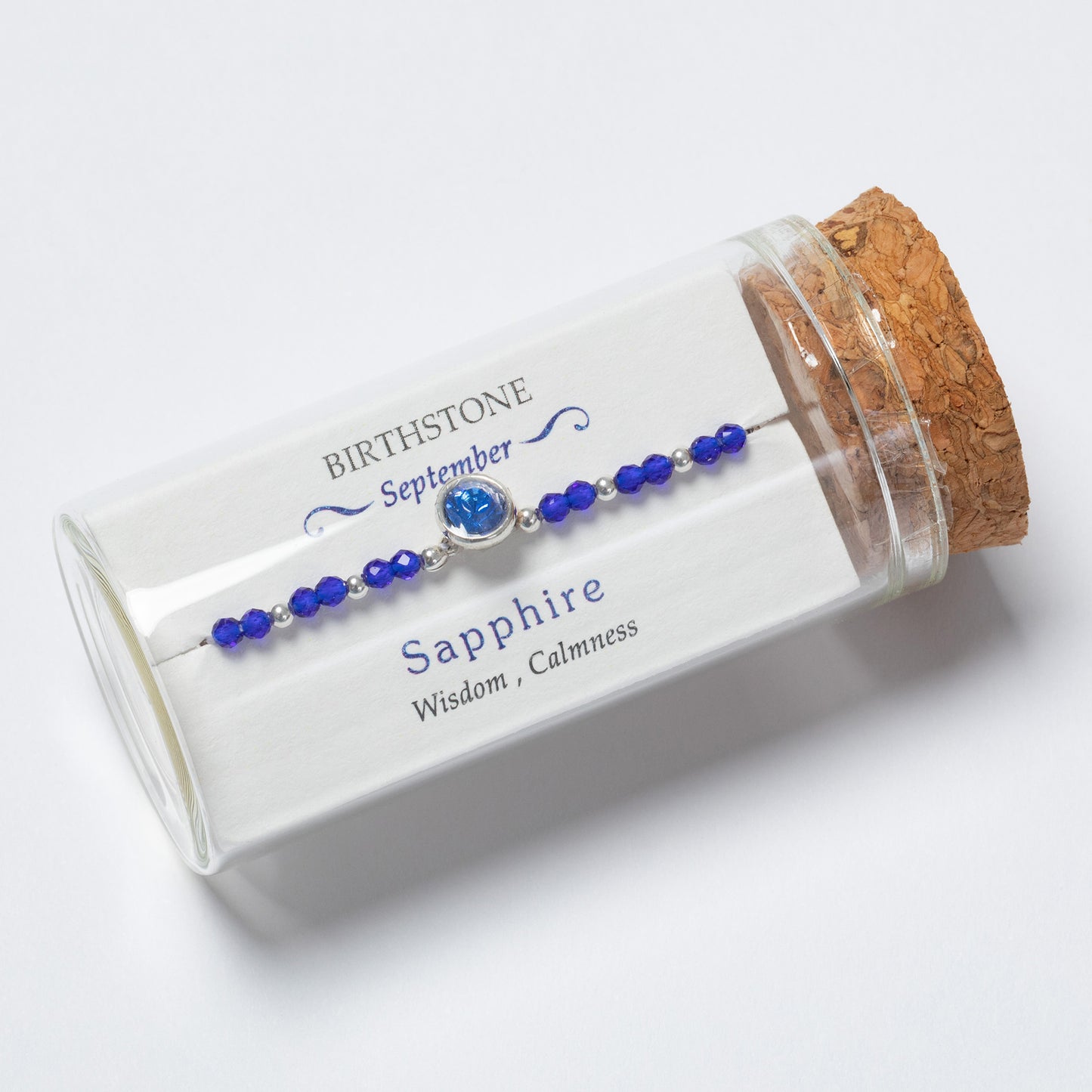 Sapphire bracelet in a clear cylindrical container with cork lid on a white background