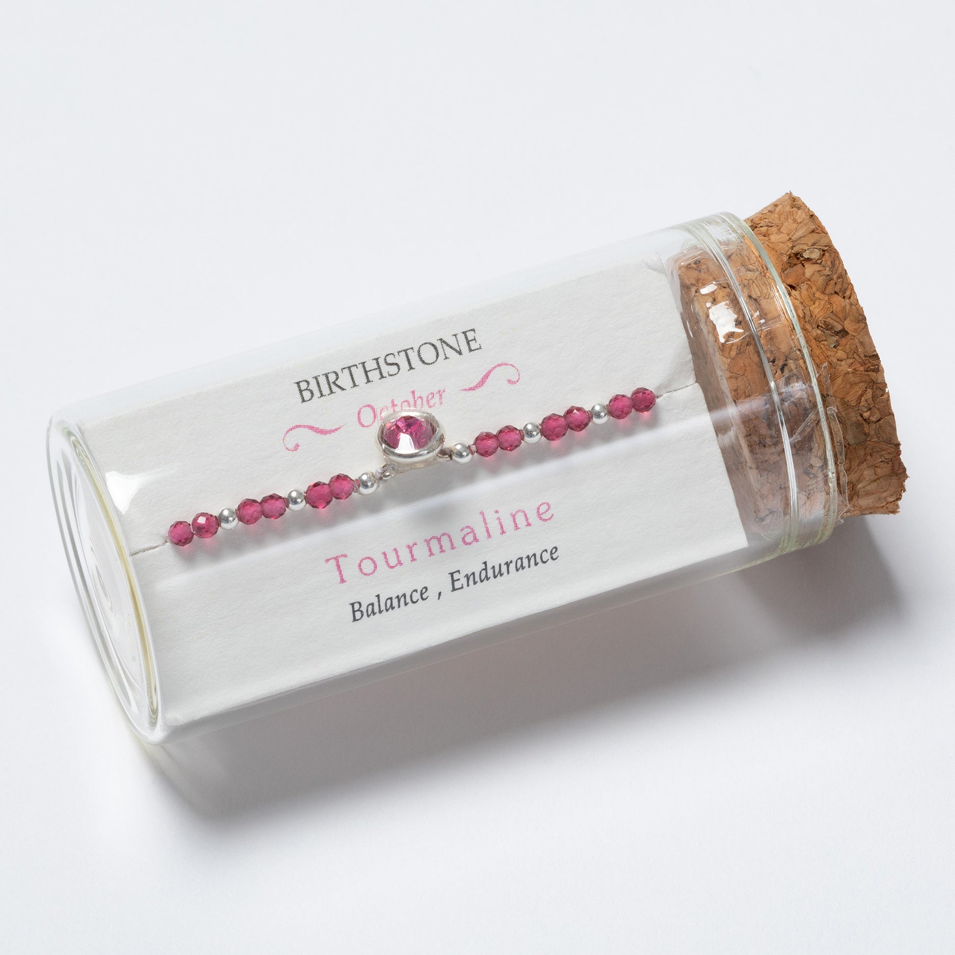 Pink beaded bracelet in a glass tube with cork lid on a white background