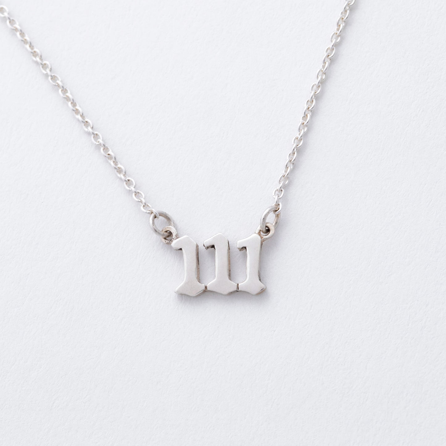 Silver necklace with a "111" pendant on a light gray background