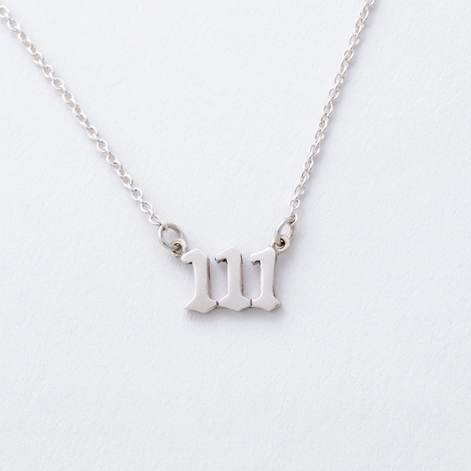 Silver necklace with a "111" pendant on a light gray background