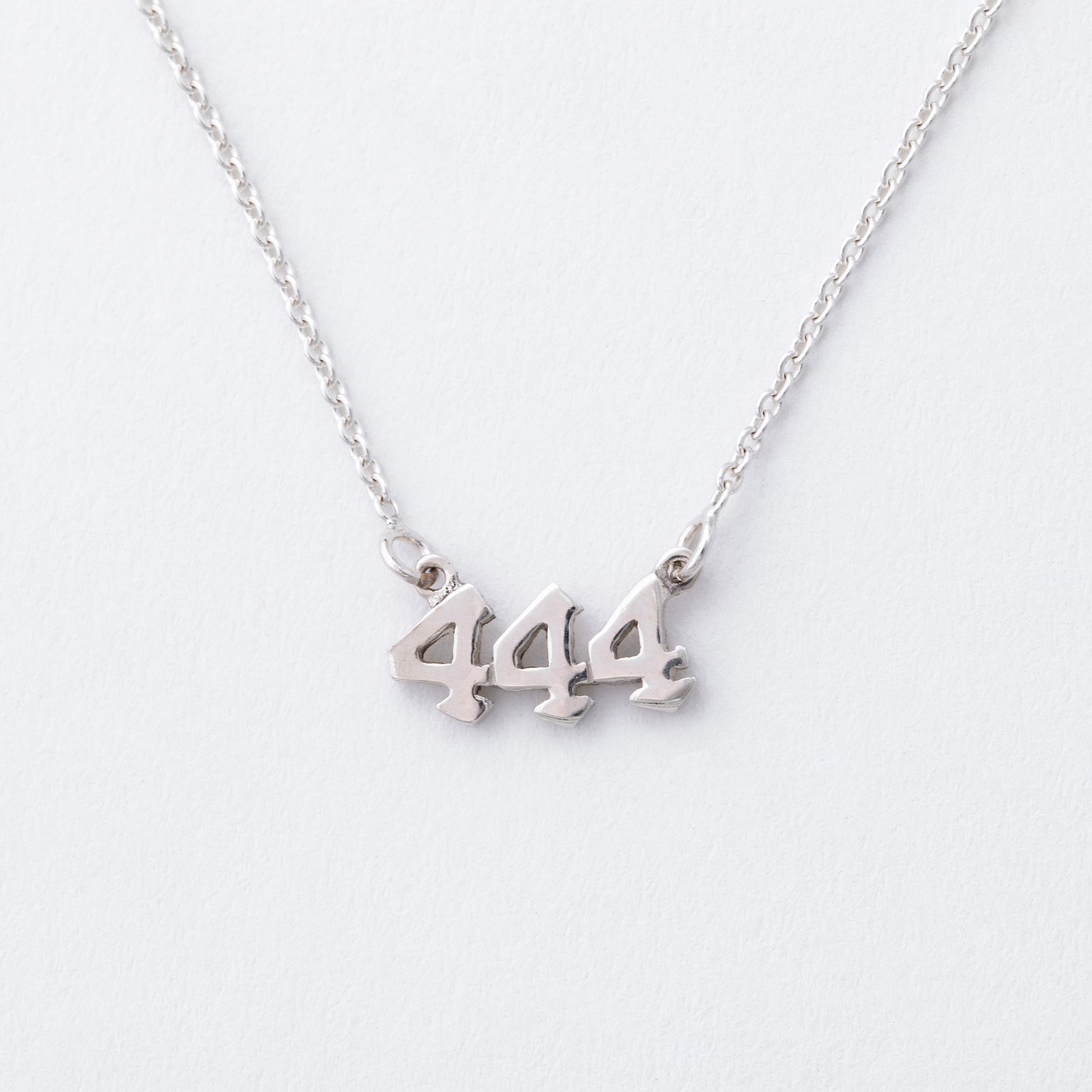 Silver necklace with '444' pendant on a white background