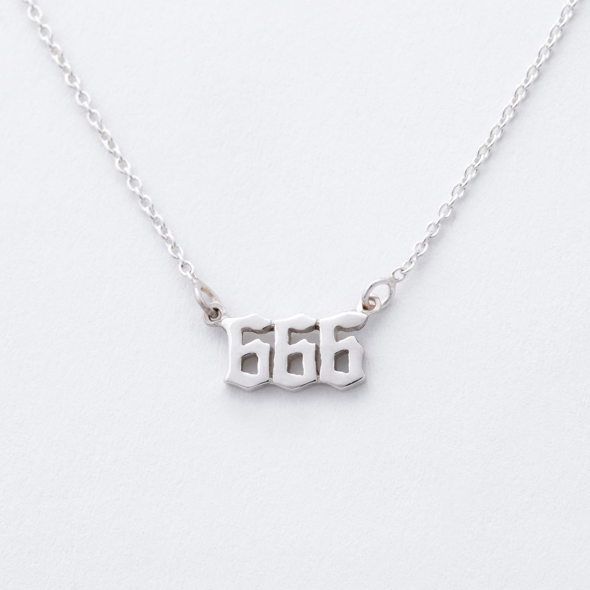 Silver necklace with '666' pendant on a white background