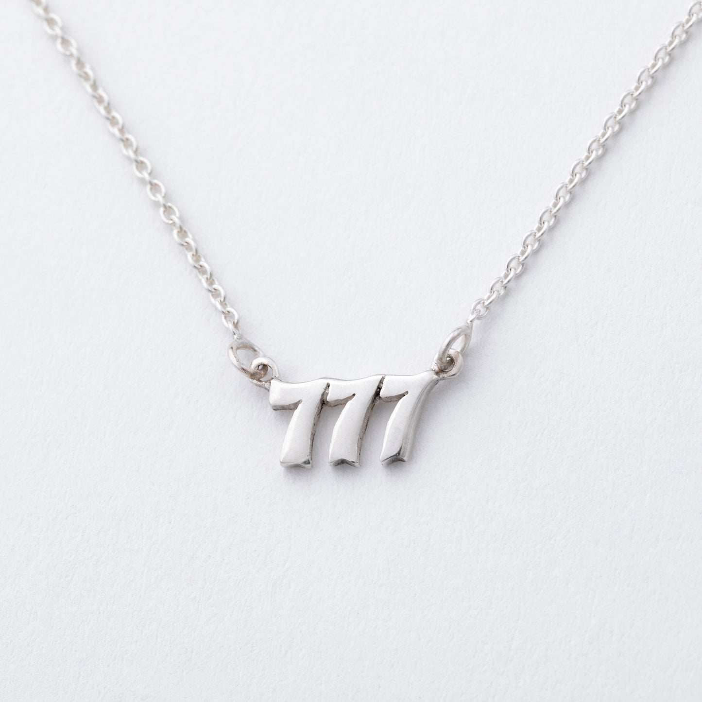 Silver necklace with the number '7' pendant on a light gray background