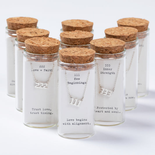 Set of glass jars with cork lids containing necklaces and inspirational messages.