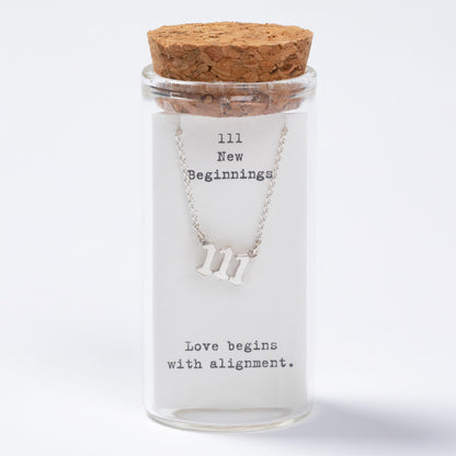 Glass jar with cork lid containing a necklace with 'III' symbol and text inside.