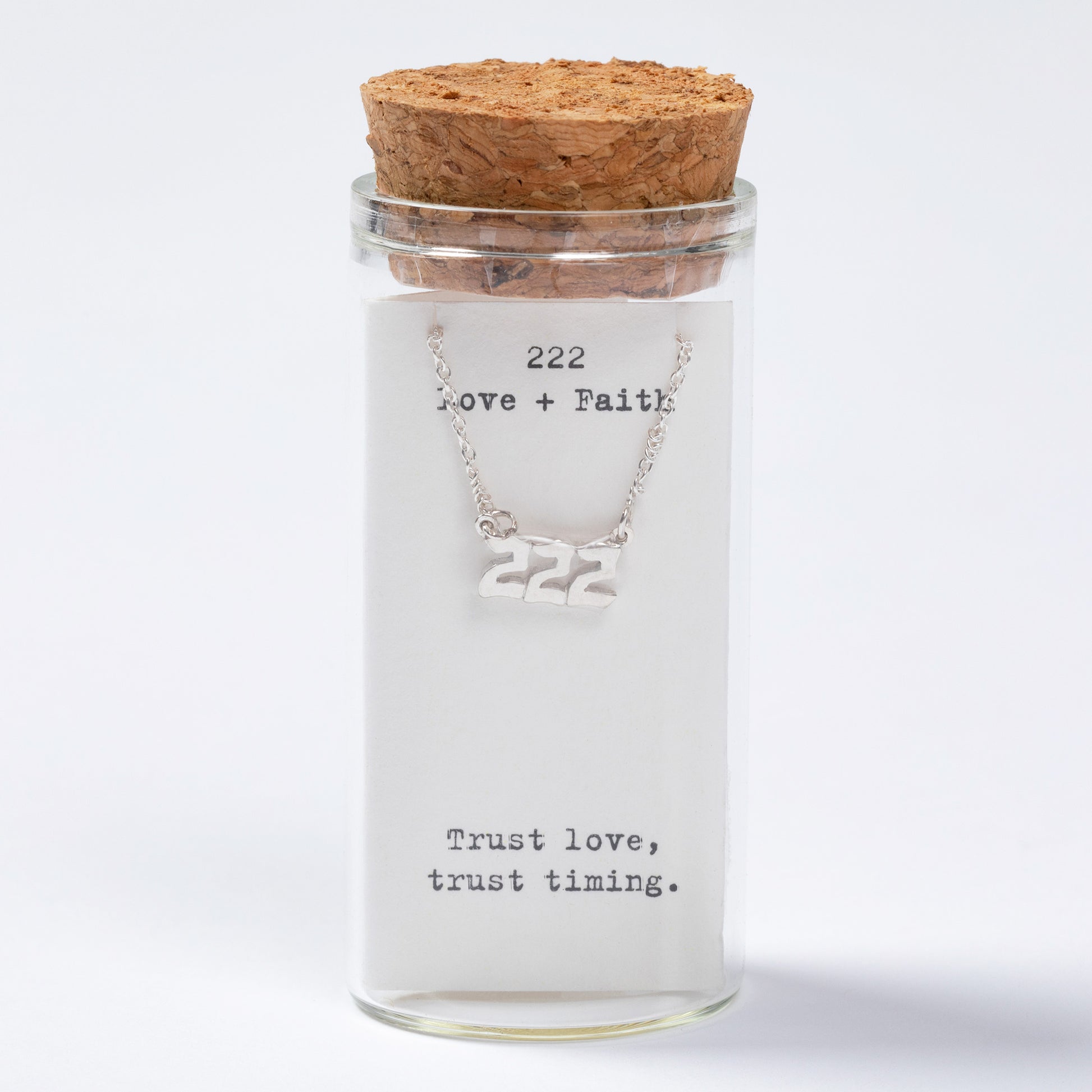 Glass jar with cork lid containing a necklace with '222' on a white background