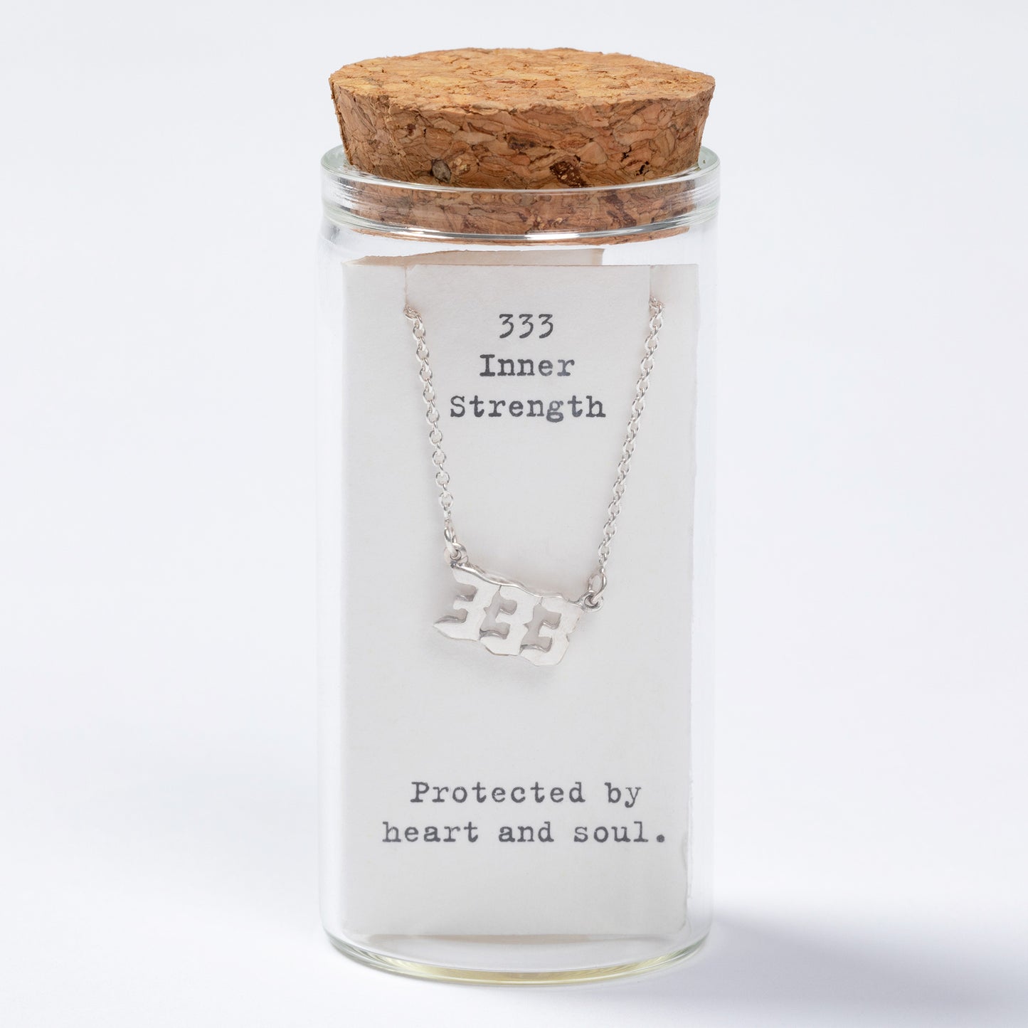 Glass jar with cork lid containing a necklace labeled '333 Inner Strength, Protected by heart and soul' on a white background
