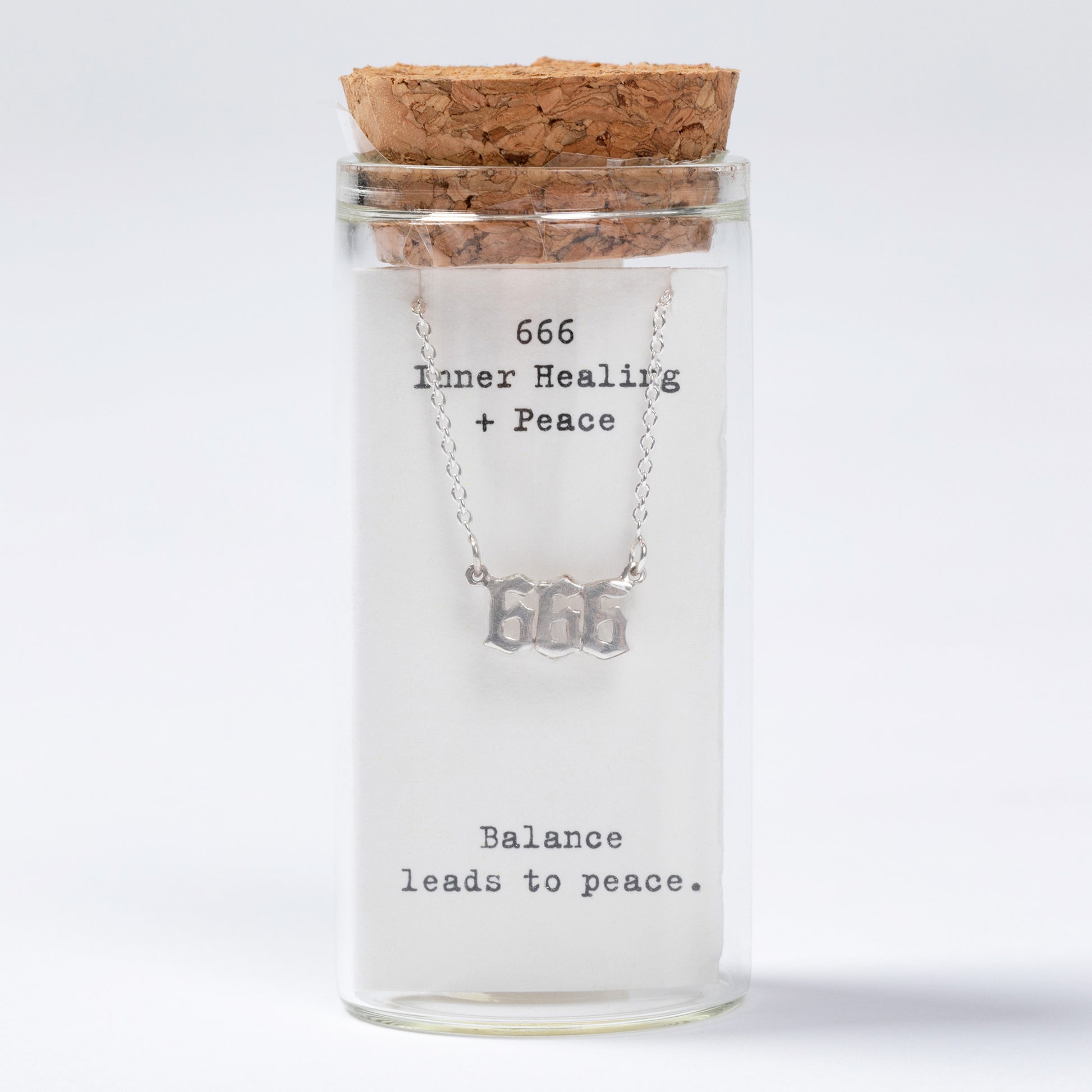 Glass jar with cork lid containing a necklace labeled '666 Inner Healing + Peace Balance leads to peace' on a white background.