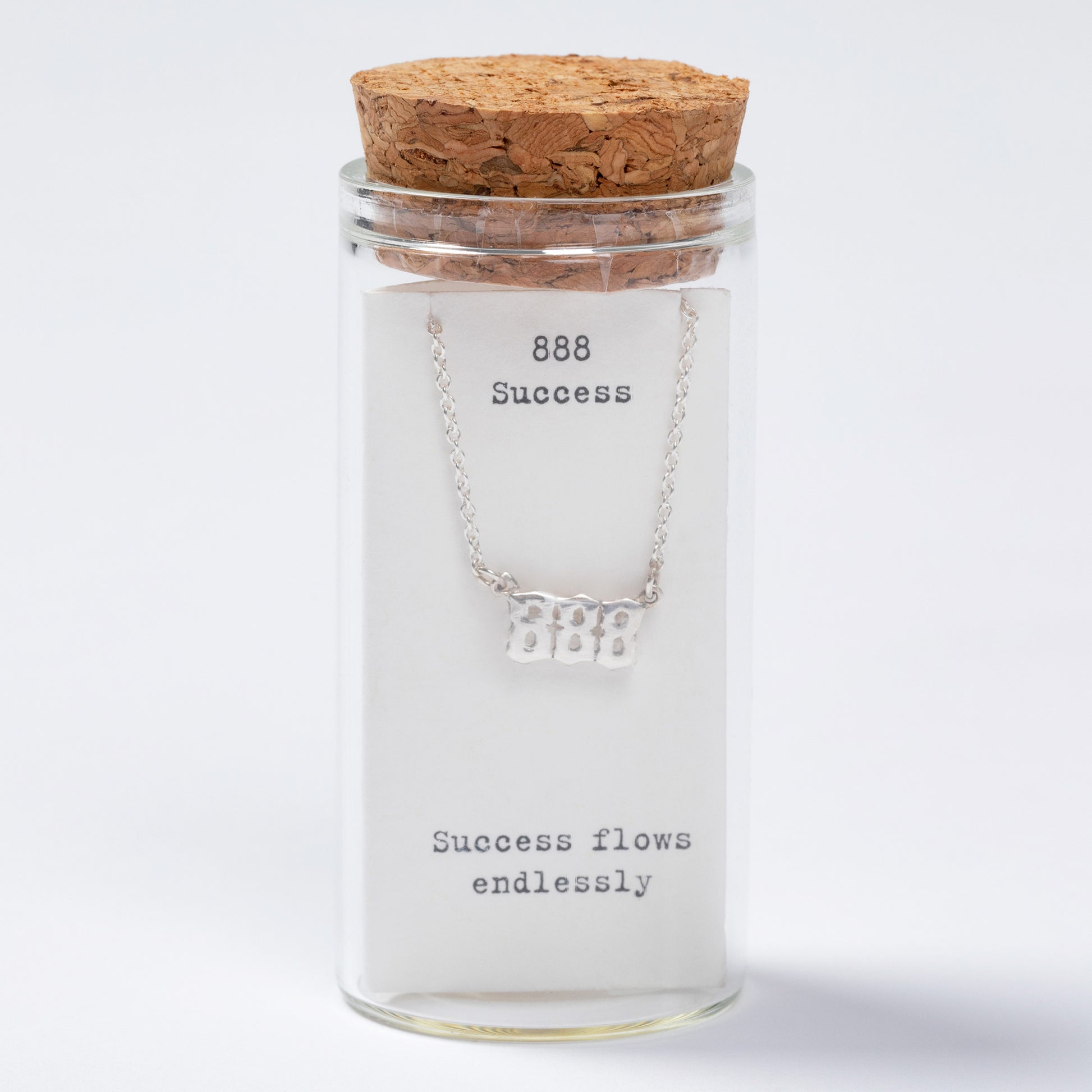 Glass jar with cork lid containing a silver necklace with '888 Success' engraving on a white background.