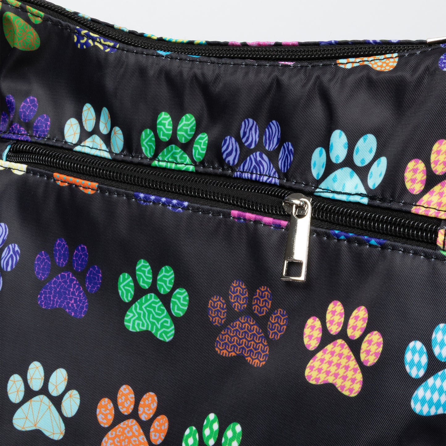 Close-up of a black nylon bag featuring a colorful pattern of dog paw prints in various colors and textures, with a black zipper and silver metal pull.