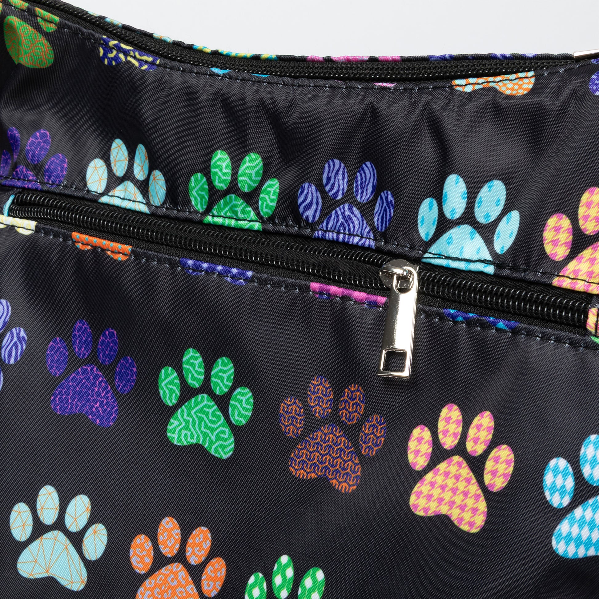 Close-up of a black nylon bag featuring a colorful pattern of dog paw prints in various colors and textures, with a black zipper and silver metal pull.