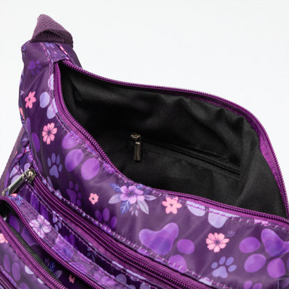 Close-up of a purple patterned bag with a floral and paw print design, showing the black interior lining and zipper compartments.