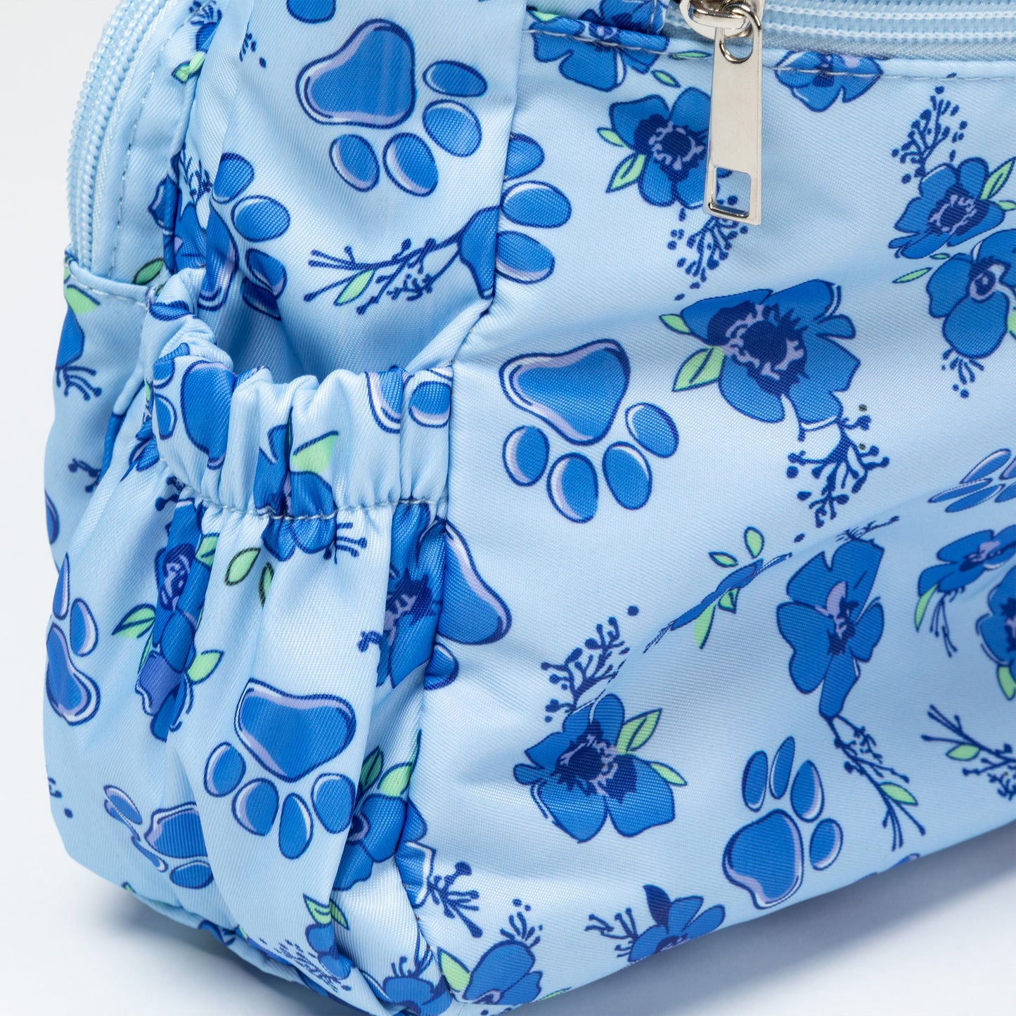 A light blue zippered pouch featuring a blue paw print and floral pattern, with a silver zipper pull.