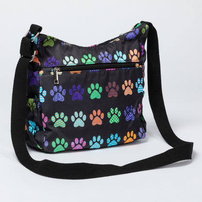 A black nylon shoulder bag with a colorful dog paw print pattern, featuring a front zippered pocket and a black adjustable shoulder strap, shown on a light gray background.