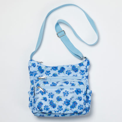 A light blue crossbody bag with a medium blue floral pattern, featuring multiple zippered pockets and an adjustable shoulder strap, shown against a plain white background.