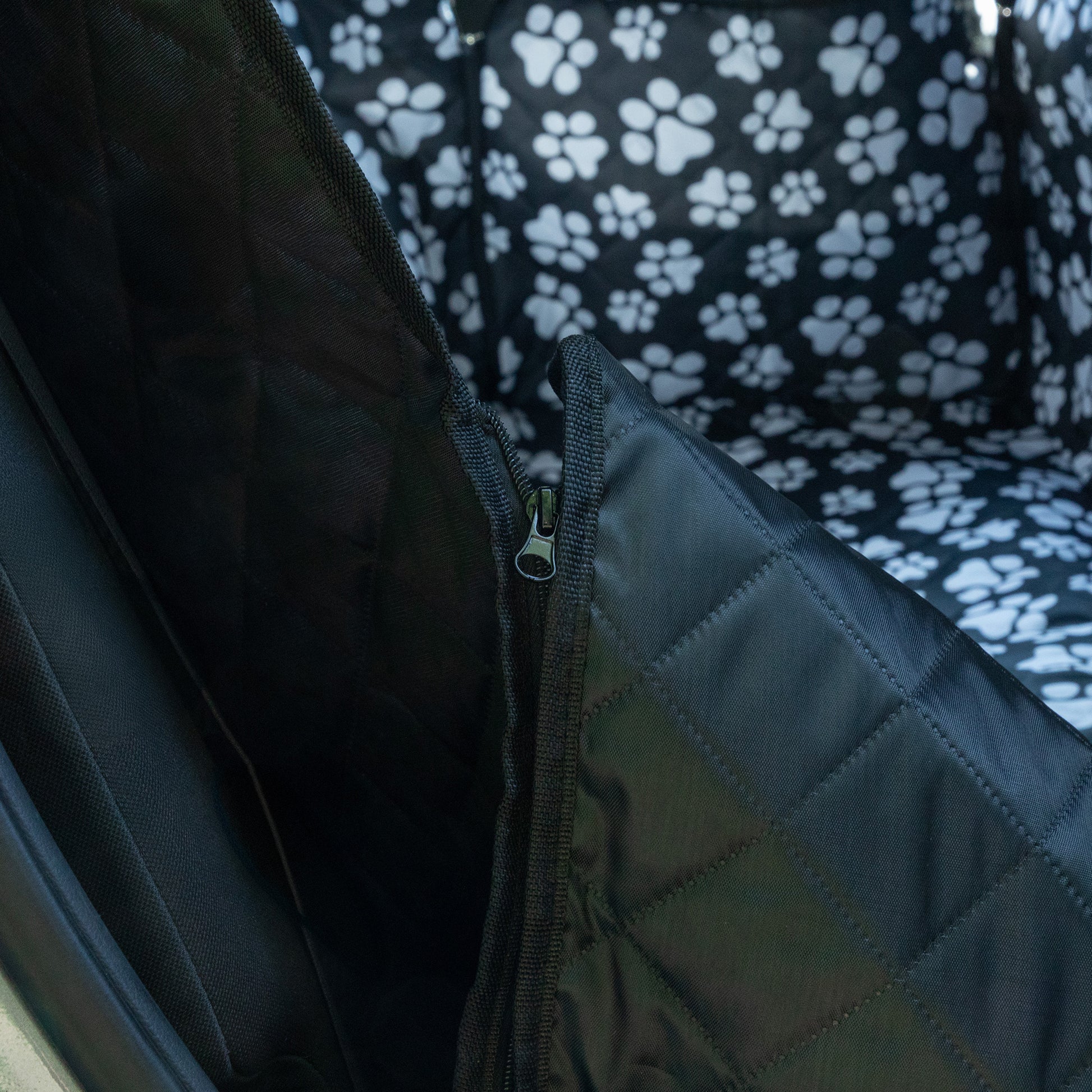 Close-up of a quilted fabric with a zipper, featuring a pattern of white paw prints on a black background.