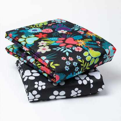 Stack of colorful floral-patterned fabric and black fabric with white paw prints on a white background