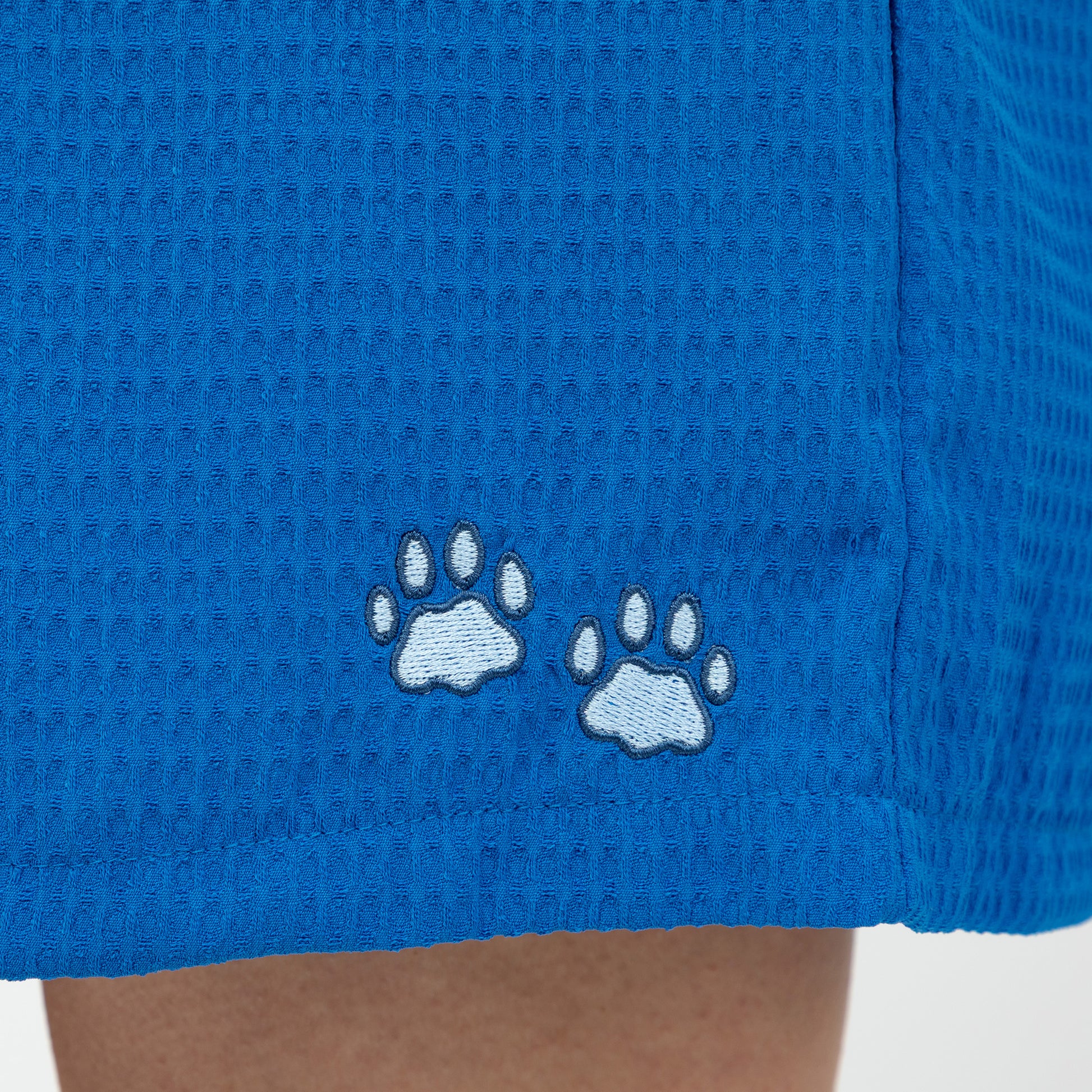 Blue shorts with embroidered light blue paw prints on a textured fabric background