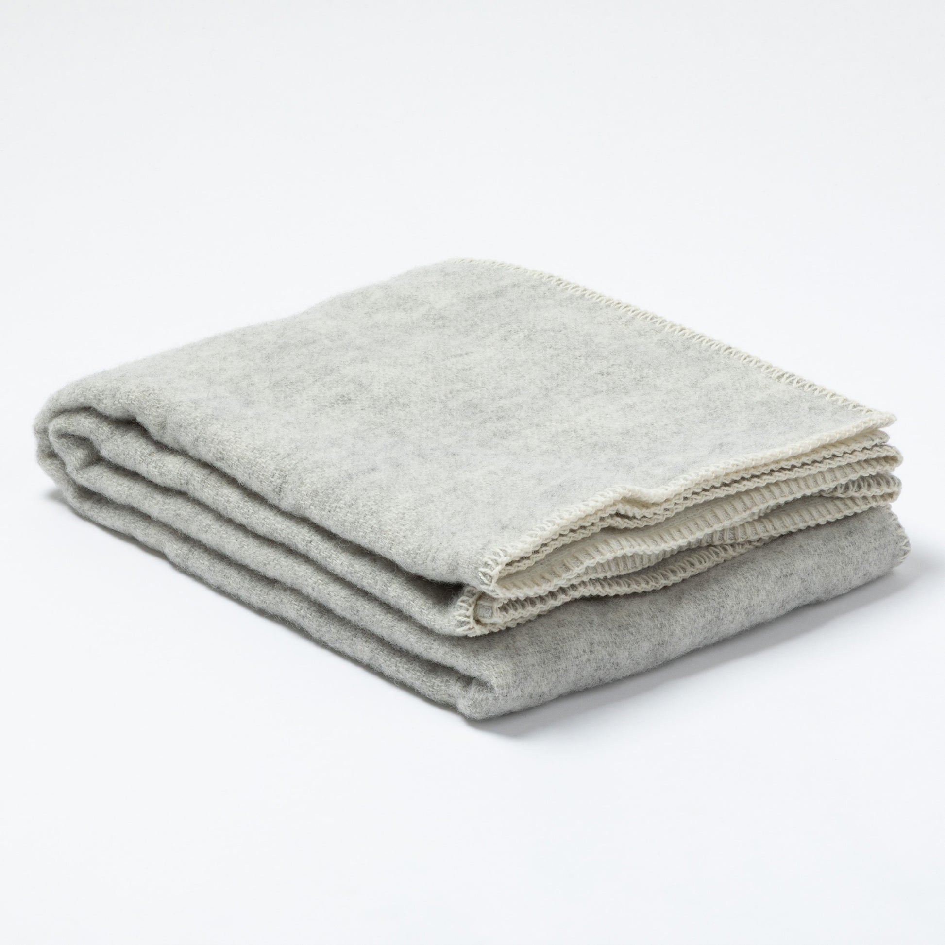 A folded light gray wool blanket with a cream-colored fringed edge, displayed on a clean white background.