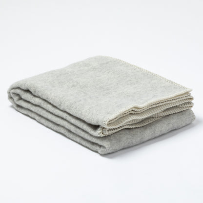 A folded light gray wool blanket with a cream-colored fringed edge, displayed on a clean white background.