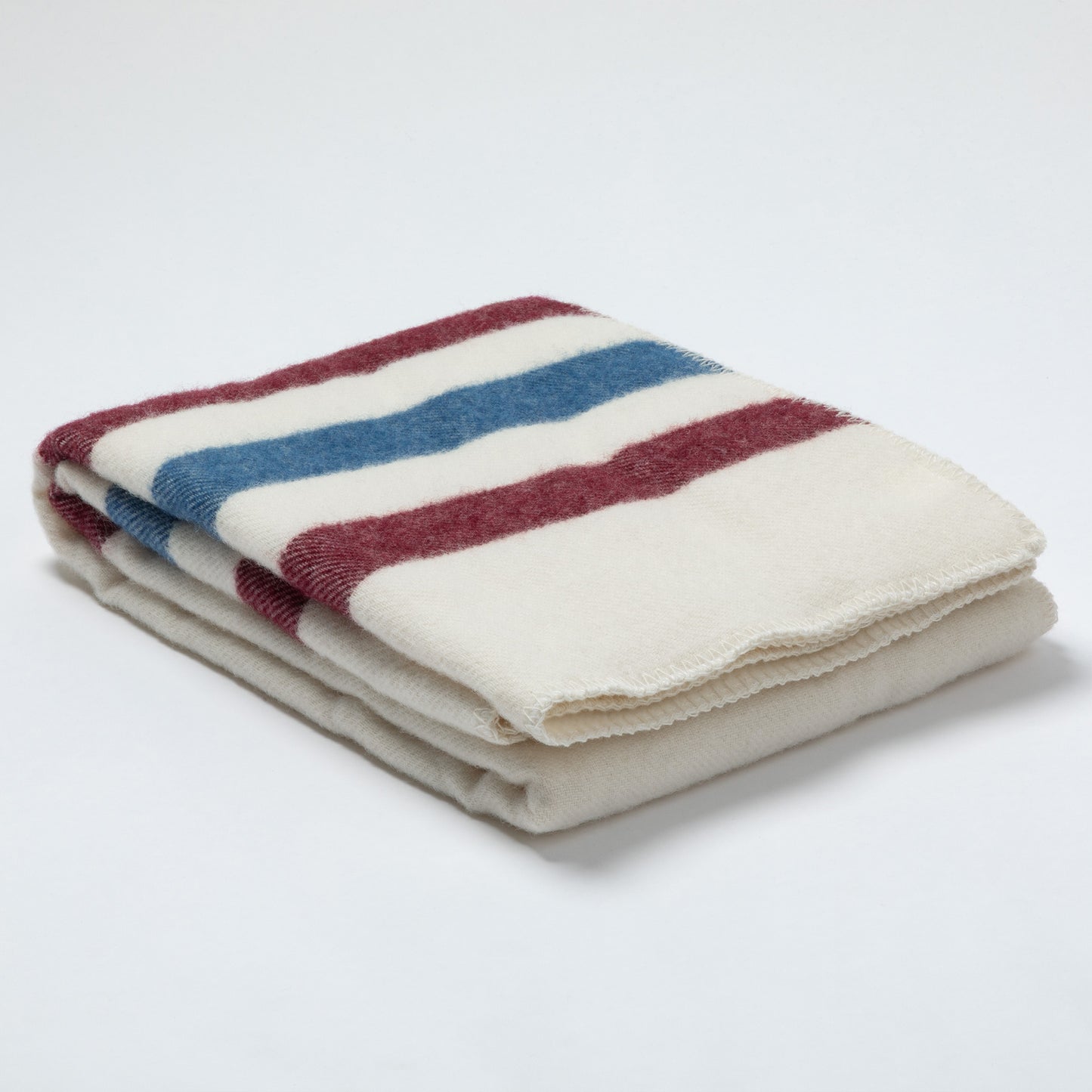 A folded cream-colored fleece blanket with horizontal stripes in maroon and blue, set against a plain white background.