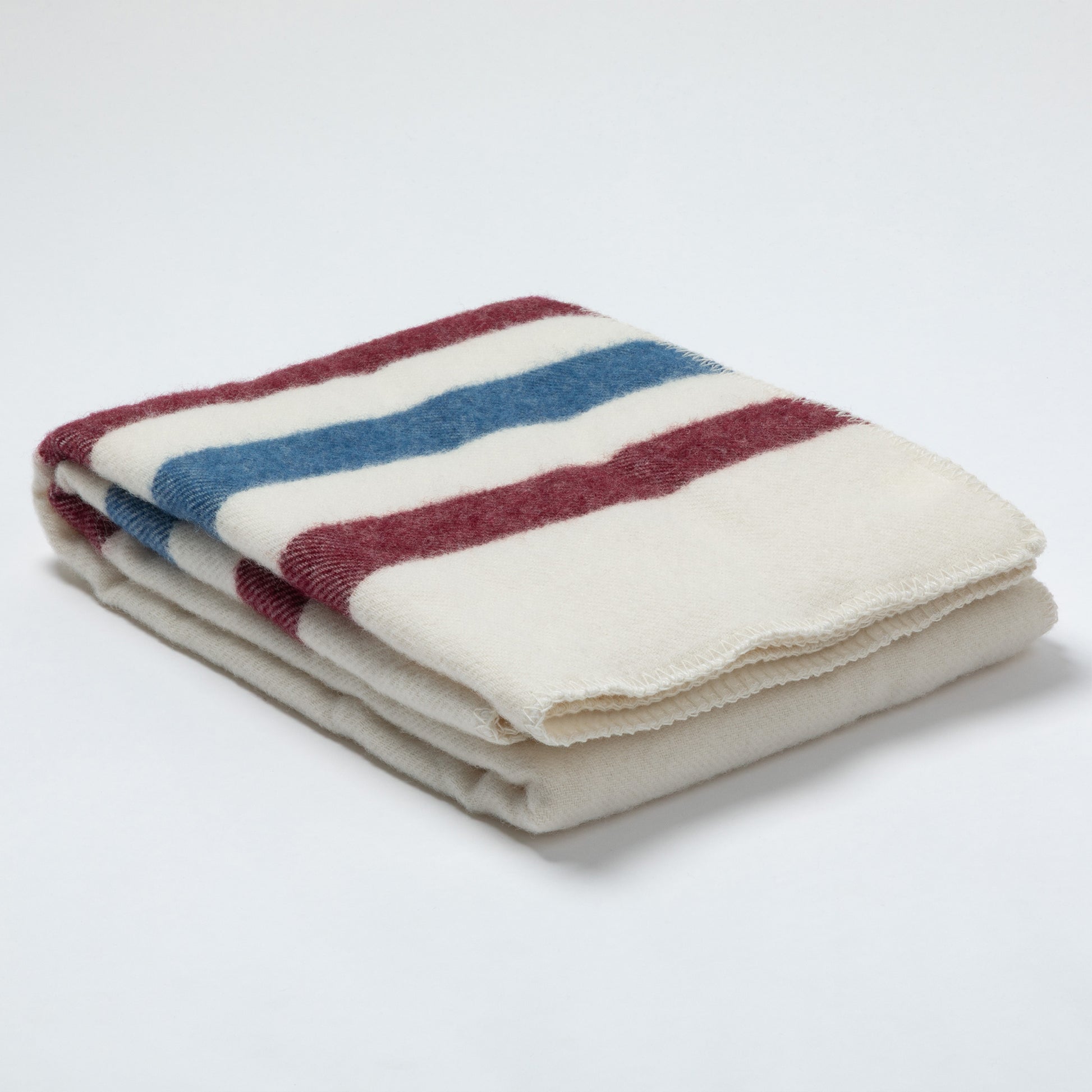 A folded cream-colored fleece blanket with horizontal stripes in maroon and blue, set against a plain white background.