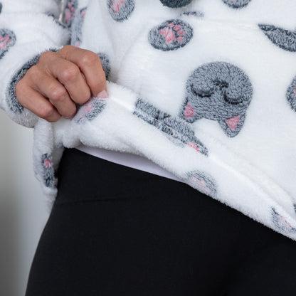 Close-up of a person wearing a white plush fleece zip-up hoodie with a gray cartoon cat face print and black leggings.
