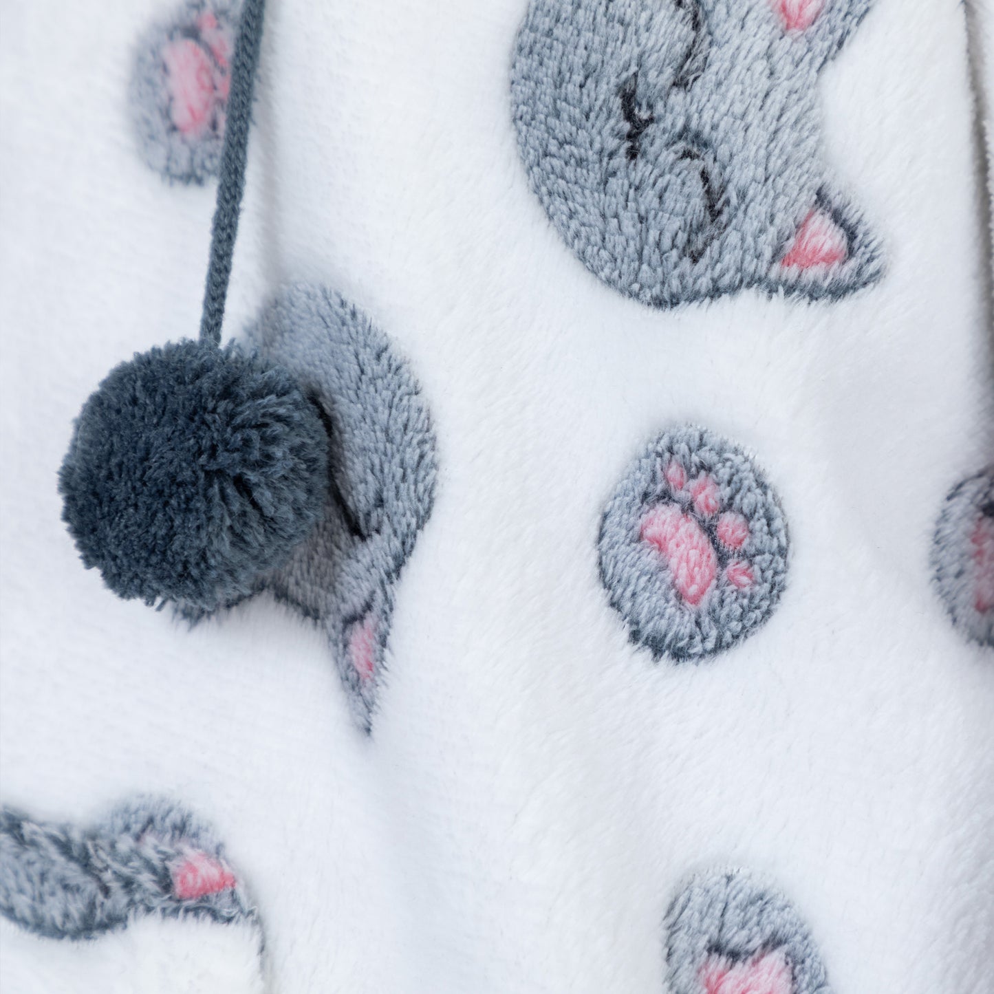 Close-up of a white plush fabric featuring a gray cat face and paw print pattern with pink paw pads, plus a gray pom-pom drawstring.