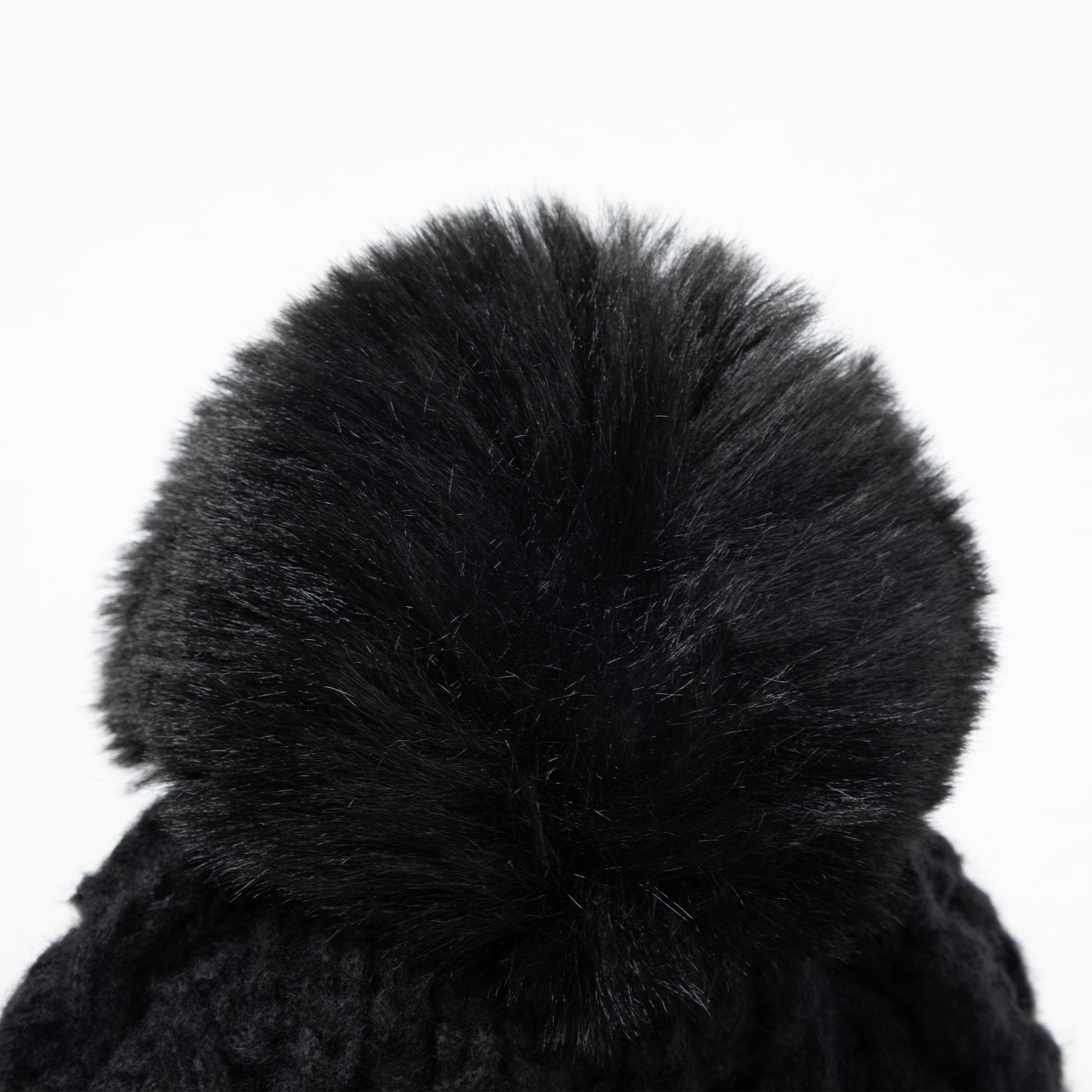 Close-up of a black knit beanie with a large fluffy faux-fur pom-pom on a plain white background.