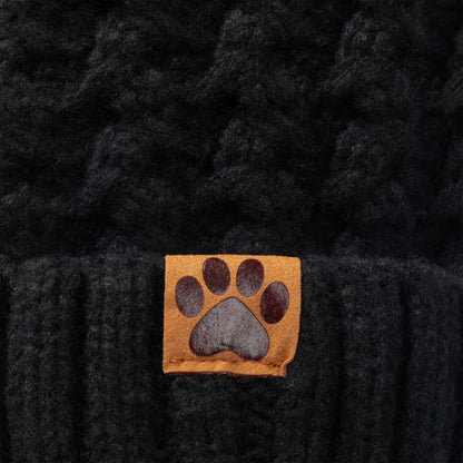 Close-up of a black textured knit beanie with a small tan square patch featuring a dark gray paw print on the front.