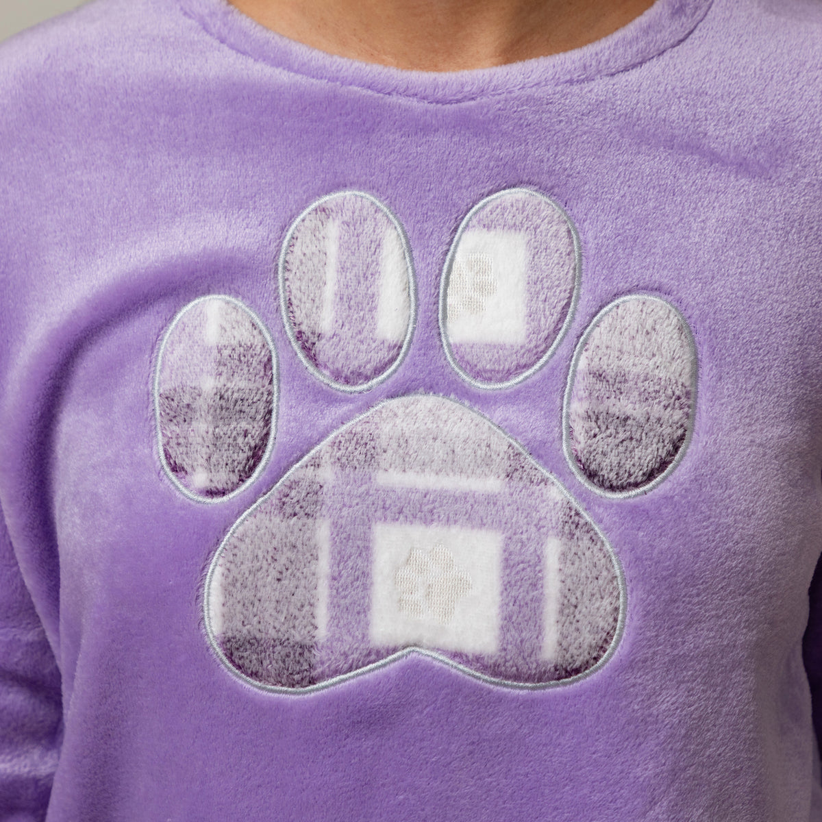 A close-up of a purple fleece pj top featuring a large paw print graphic on the front, worn by a person whose neck is visible at the top.