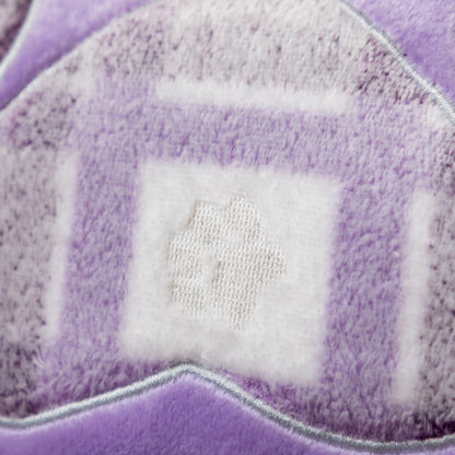 Close-up of a plush purple and white textured fabric with a small embroidered white symbol in the center.