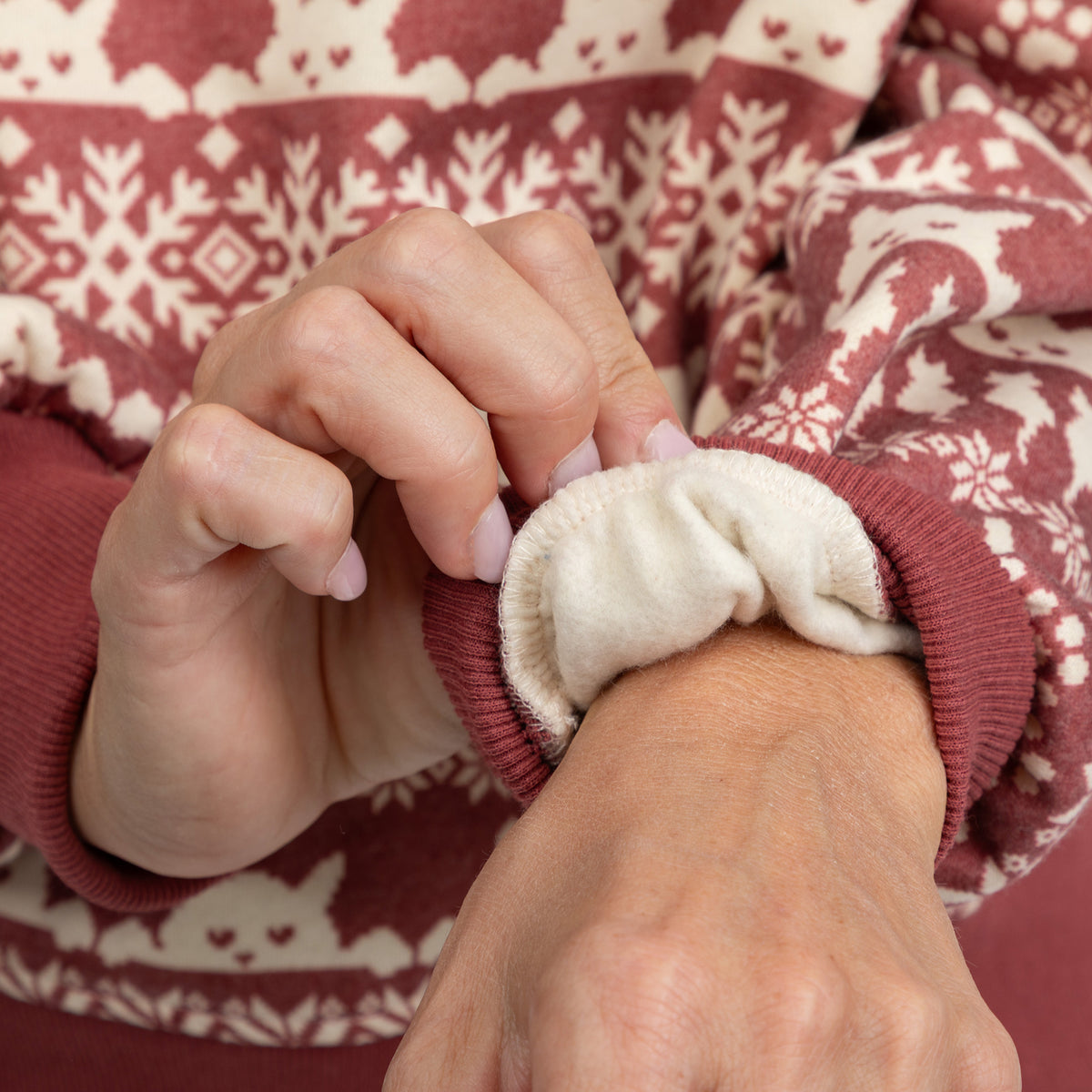 Close-up of a person's hands and wrist wearing a burgundy knit sweater with a cream pattern and a soft cream fleece lining inside the cuff.