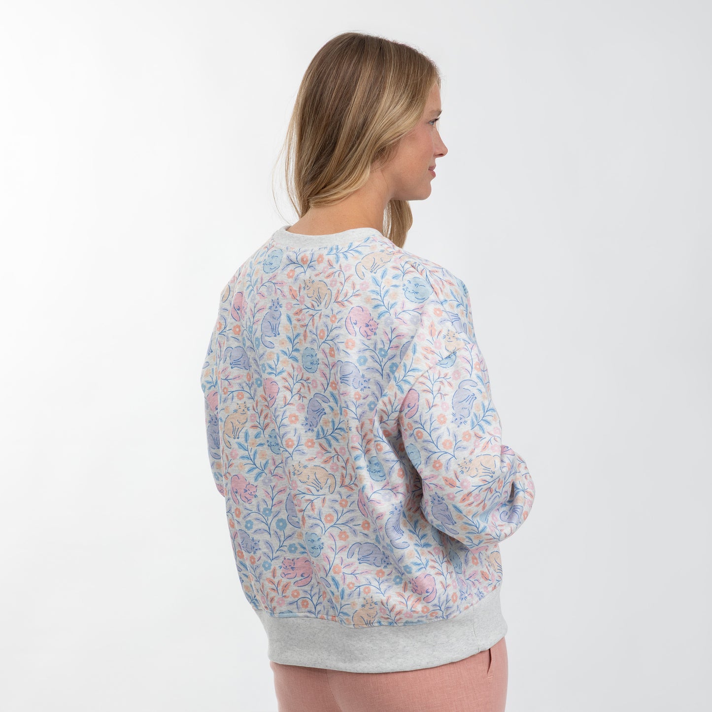 A woman shown from the back wearing a light gray crewneck sweatshirt with a pastel multicolor floral and paisley pattern, set against a plain white studio background.