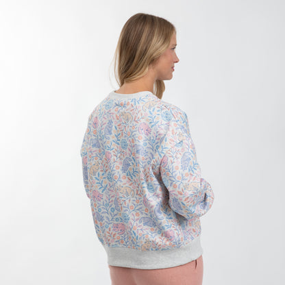 A woman shown from the back wearing a light gray crewneck sweatshirt with a pastel multicolor floral and paisley pattern, set against a plain white studio background.