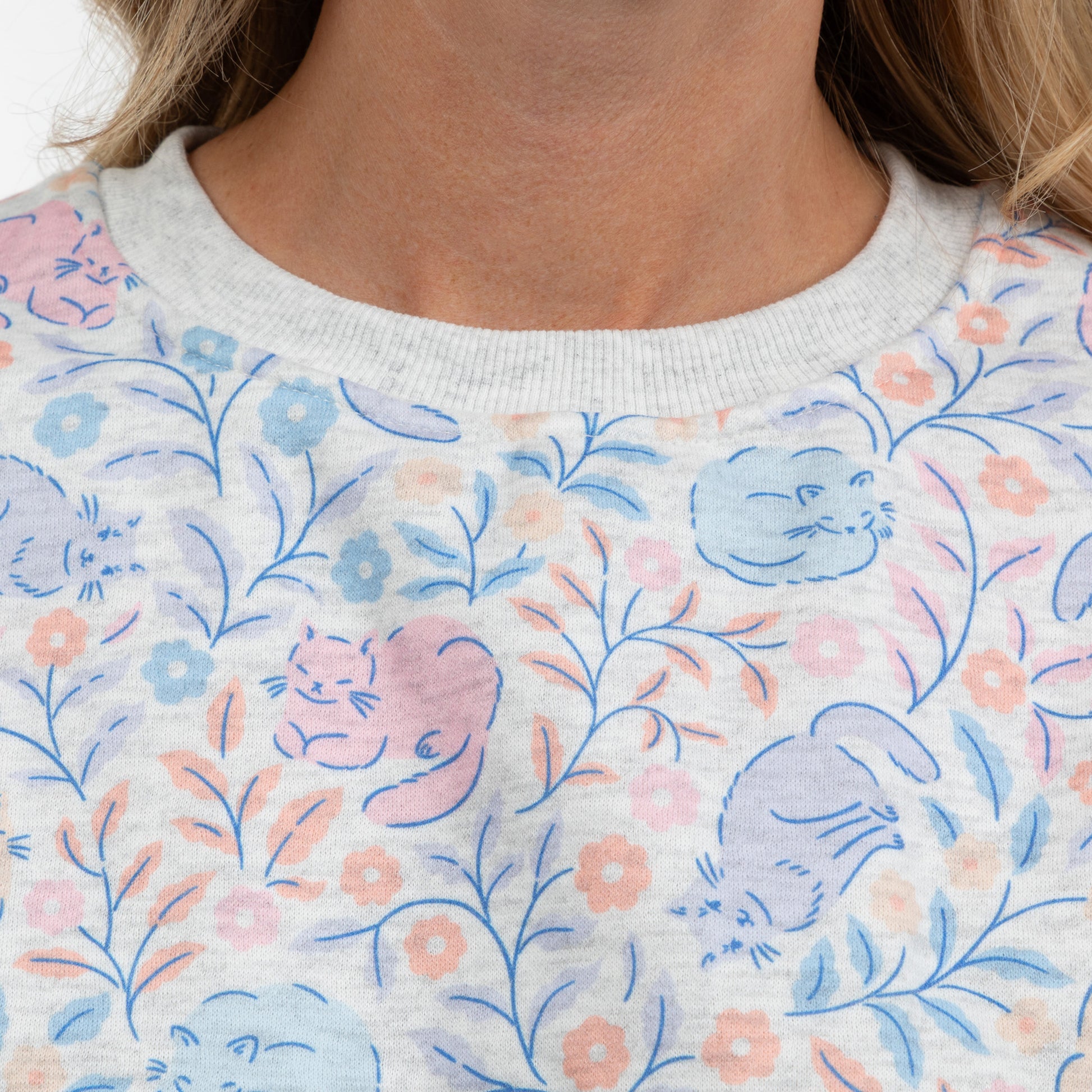 Close-up of a person wearing a light gray crewneck sweatshirt with a pastel cat and floral pattern.