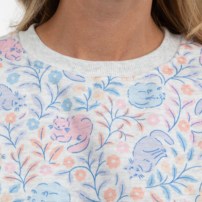 Close-up of a person wearing a light gray crewneck sweatshirt with a pastel cat and floral pattern.