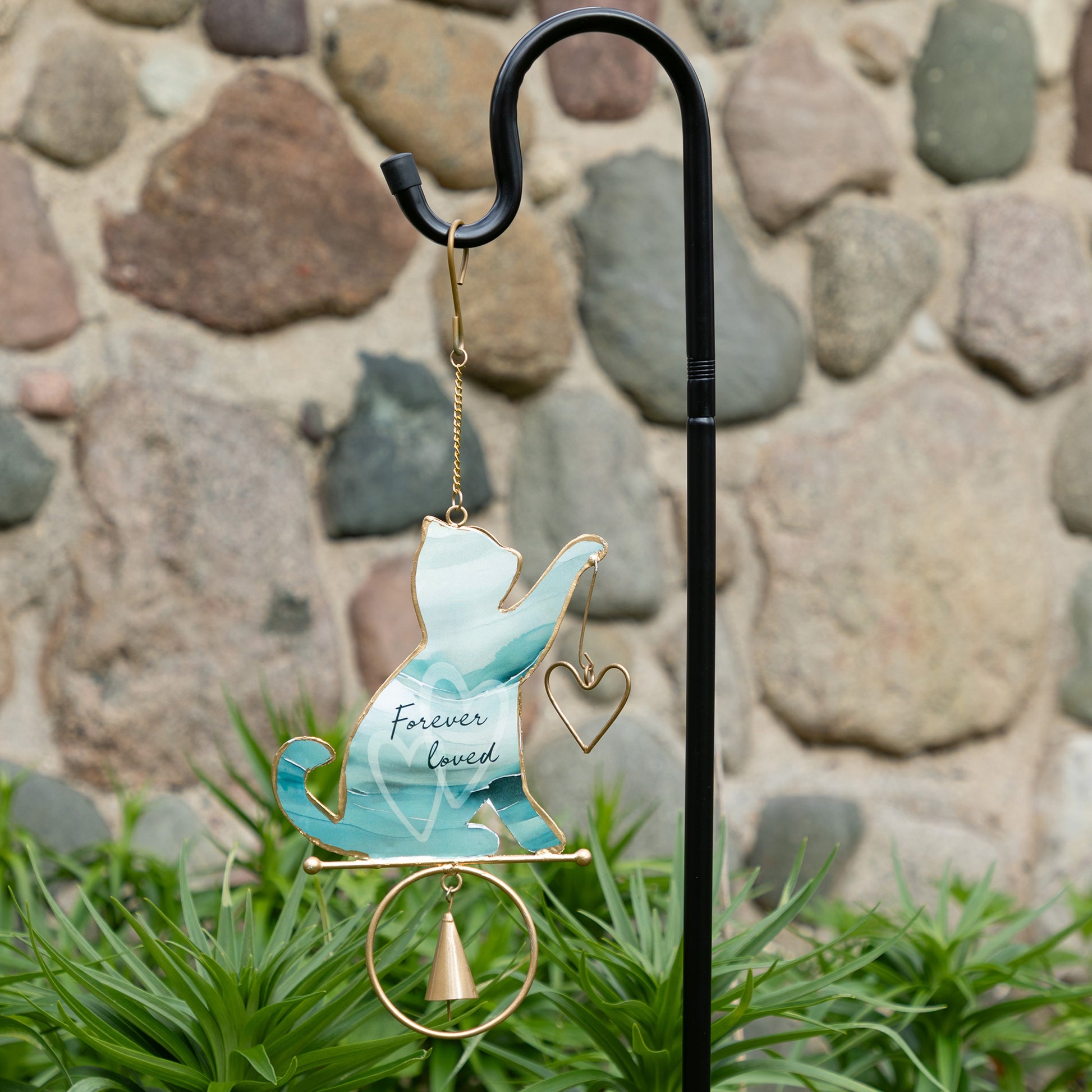 Decorative garden wind chime with a cat design and 'Forever Loved' text, against a stone wall background.