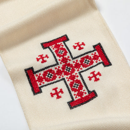 Close-up of a cream-colored woven textile featuring a large red embroidered cross with black outlines and smaller red cross motifs on a white background.