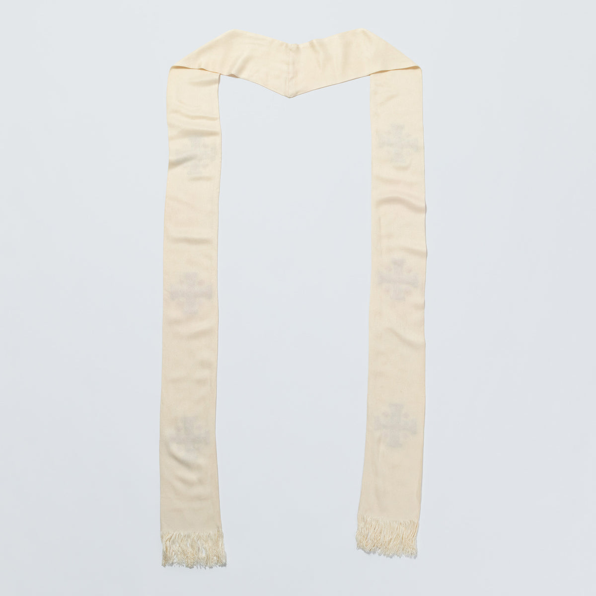A cream-colored scarf with a subtle tonal embroidered cross pattern and fringed ends, laid flat against a light gray background.