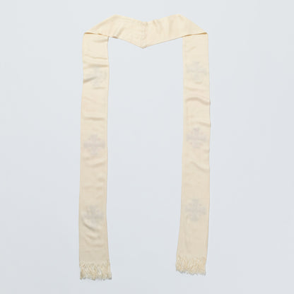 A cream-colored scarf with a subtle tonal embroidered cross pattern and fringed ends, laid flat against a light gray background.