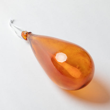 An amber glass teardrop-shaped hanging ornament with a white hanging string, photographed on a clean white background.