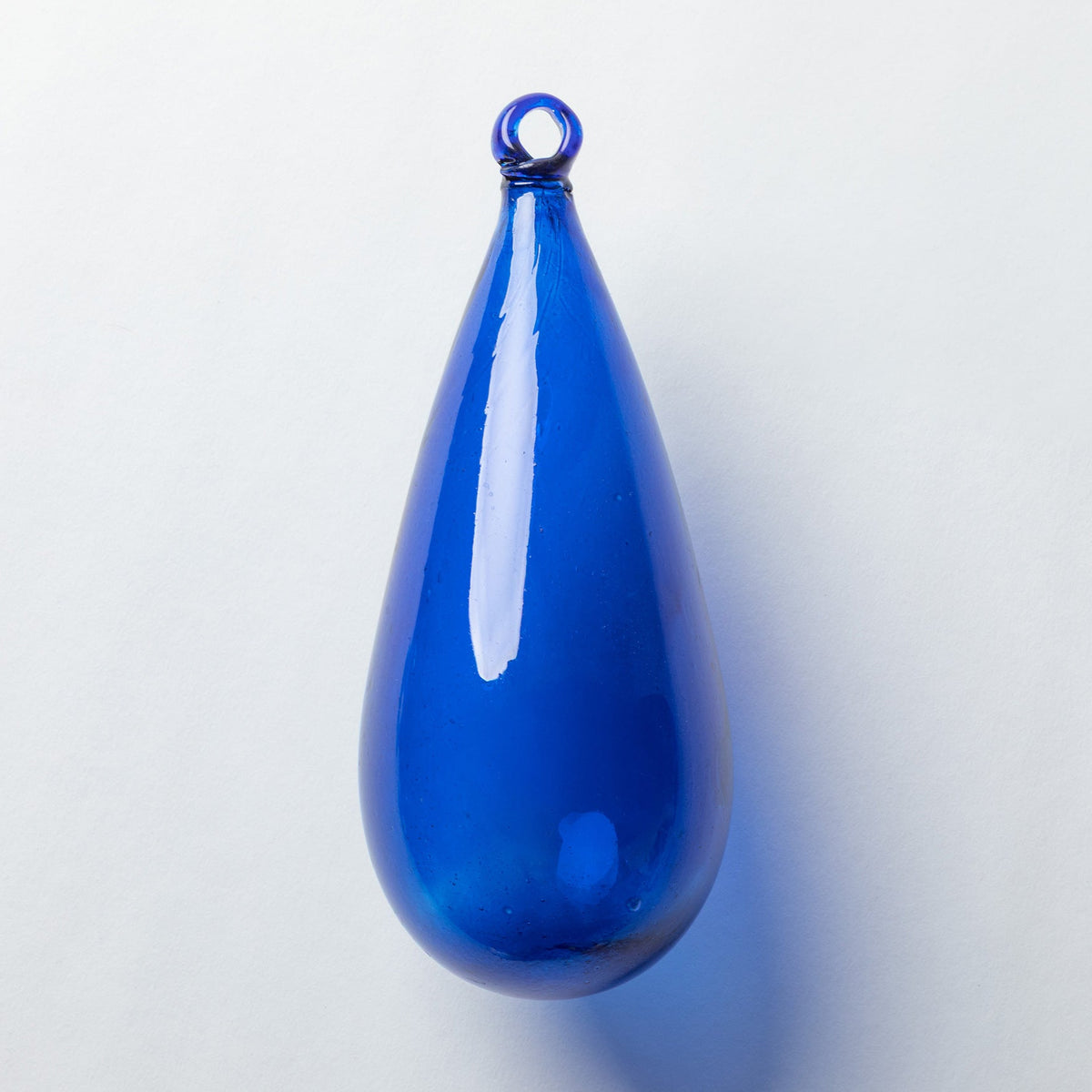 A glossy cobalt blue teardrop-shaped glass pendant with a small loop at the top, shown on a clean white background.