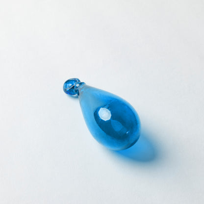 A translucent blue glass teardrop pendant with a small faceted blue top loop, photographed on a clean white background with a soft shadow.
