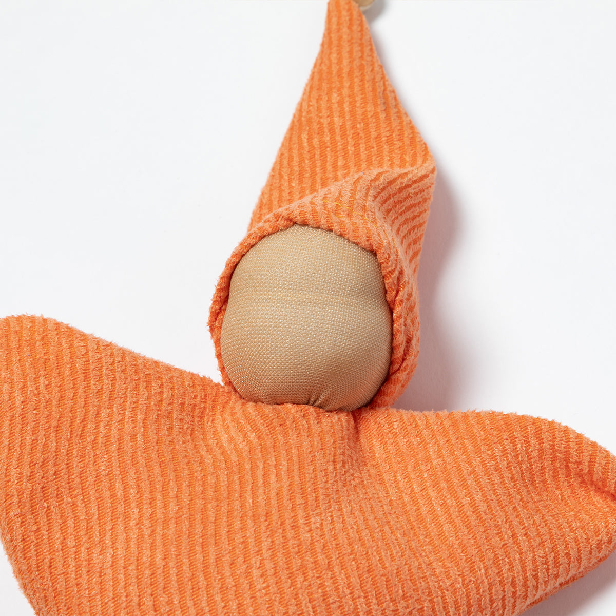 An orange ribbed fabric doll with a wooden pom-pom on the tip of the hat, a wooden pom-pom on the bottom corner, and a small white tag attached.