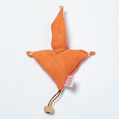 An orange ribbed fabric doll with a wooden pom-pom on the tip of the hat, a wooden pom-pom on the bottom corner, and a small white tag attached.