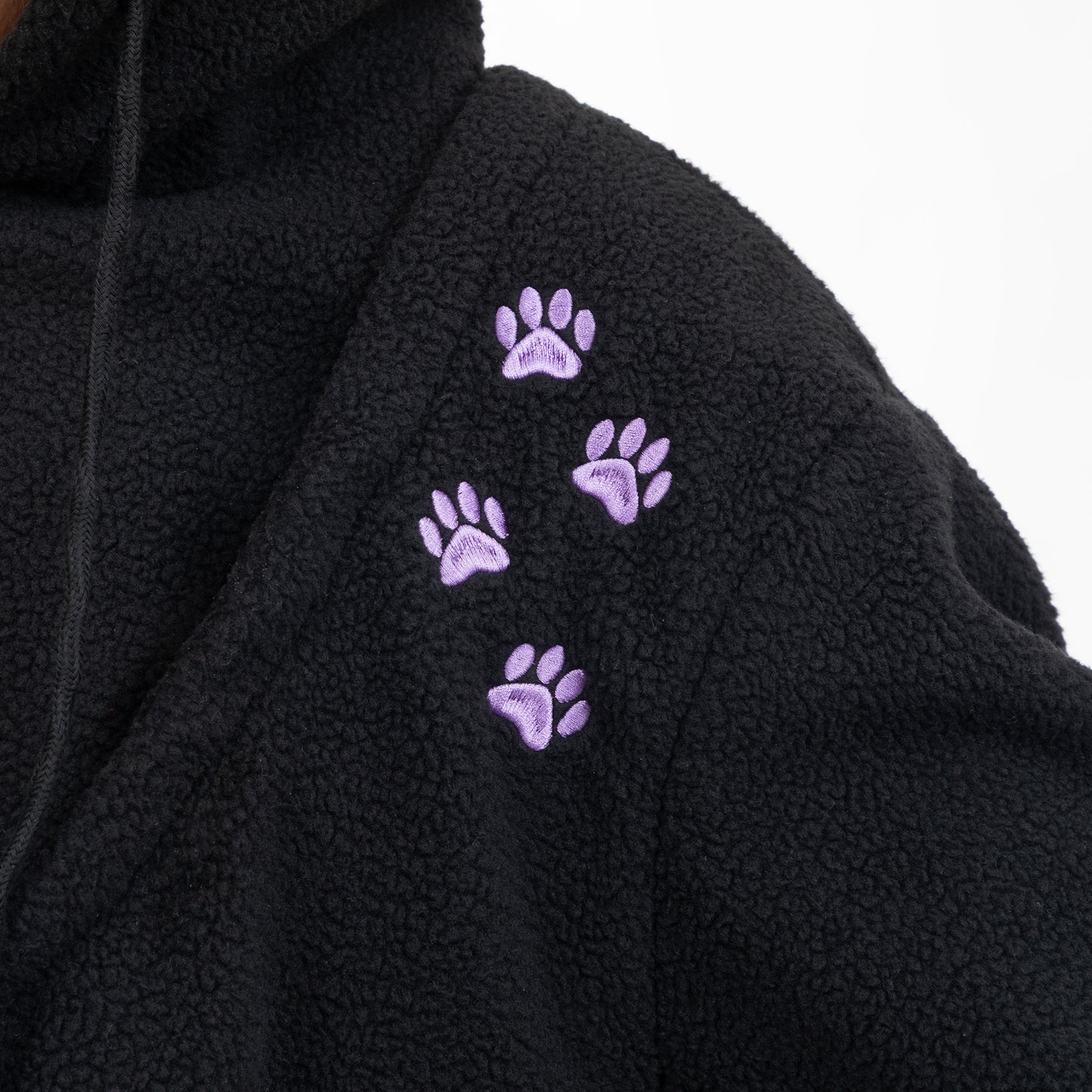 Close-up of a black sherpa fleece hoodie featuring four embroidered purple paw prints on the shoulder, set against a plain white background.