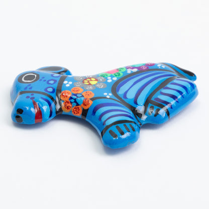 A blue ceramic magnet shaped like a dog, decorated with colorful hand-painted patterns, and black stripes set against a plain white background.