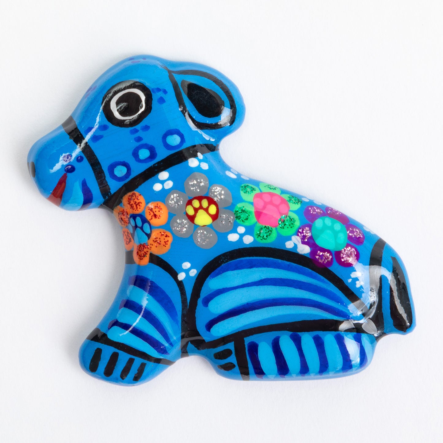 A blue ceramic magnet shaped like a dog, decorated with colorful hand-painted patterns, and black stripes set against a plain white background.